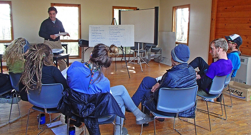 A group of students sit in chairs listening to an instructor during a wilderness first aid certification course. 